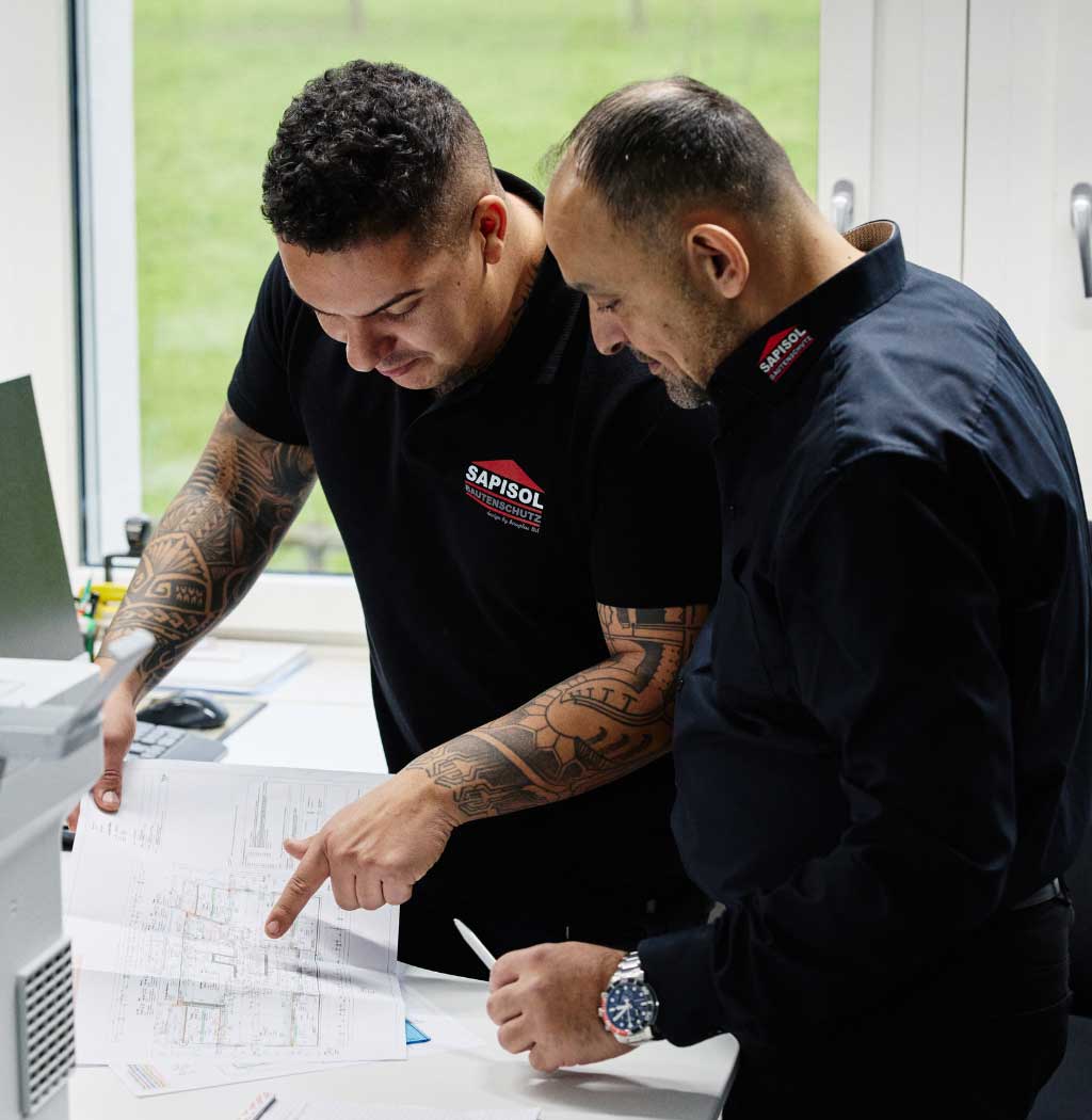 Zwei Männer betrachten gemeinsam ein Dokument, das auf einem Tisch liegt.